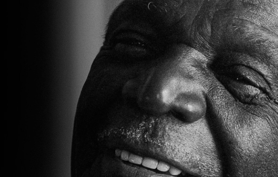 Homem negro, retratado em preto e branco, sorrindo. 
